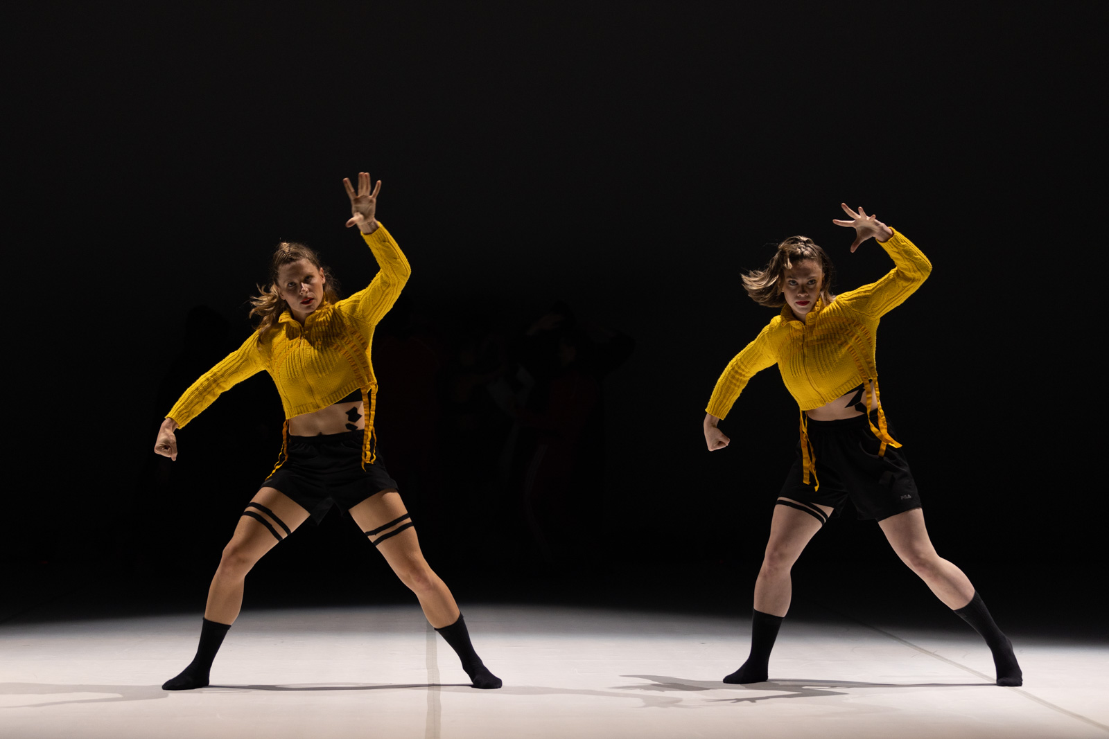Two dancers dressed in yellow and black are holding their fists high.