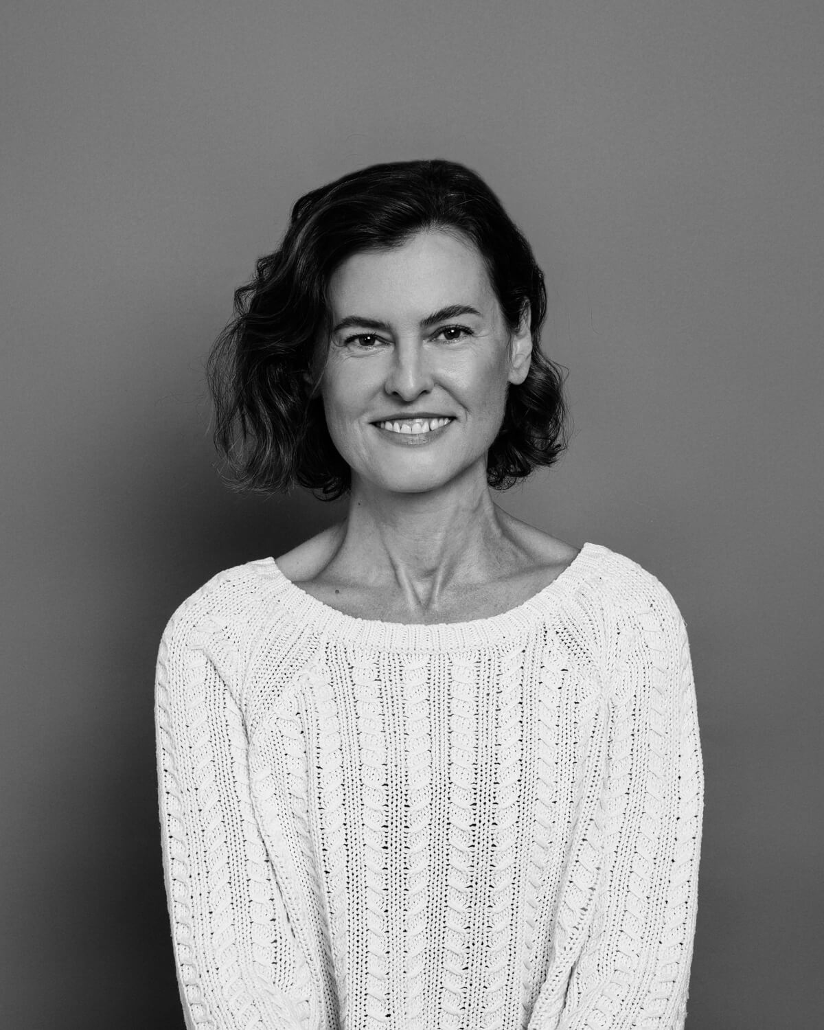 Image of Sydney Dance Company Pilates Instructor Anna Harrison smiling. She is wearing a white sweater and has short brown hair.