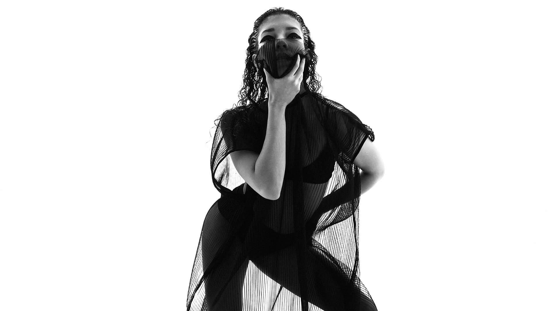 Black and white photo of a female dancer, in black, striking a pose facing the camera.