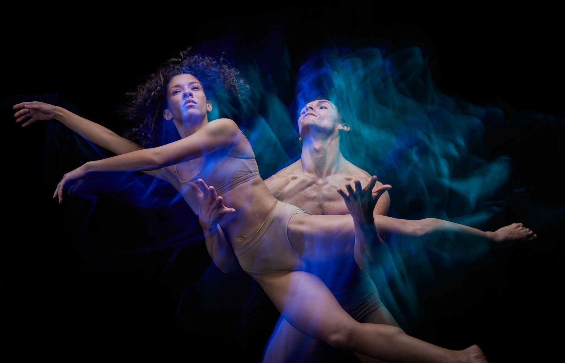 Company Dancer Naiara de Matos leaps into the air held by Riley Fitzgerald. They are bathed in soft blue light.
